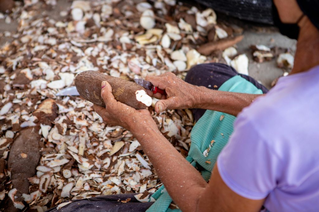A woman expertly peels cassava root, surrounded by cassava peels, for culinary preparation.