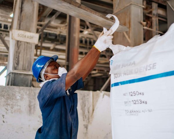 Industrial worker checking a large soda ash bag in a manufacturing facility.